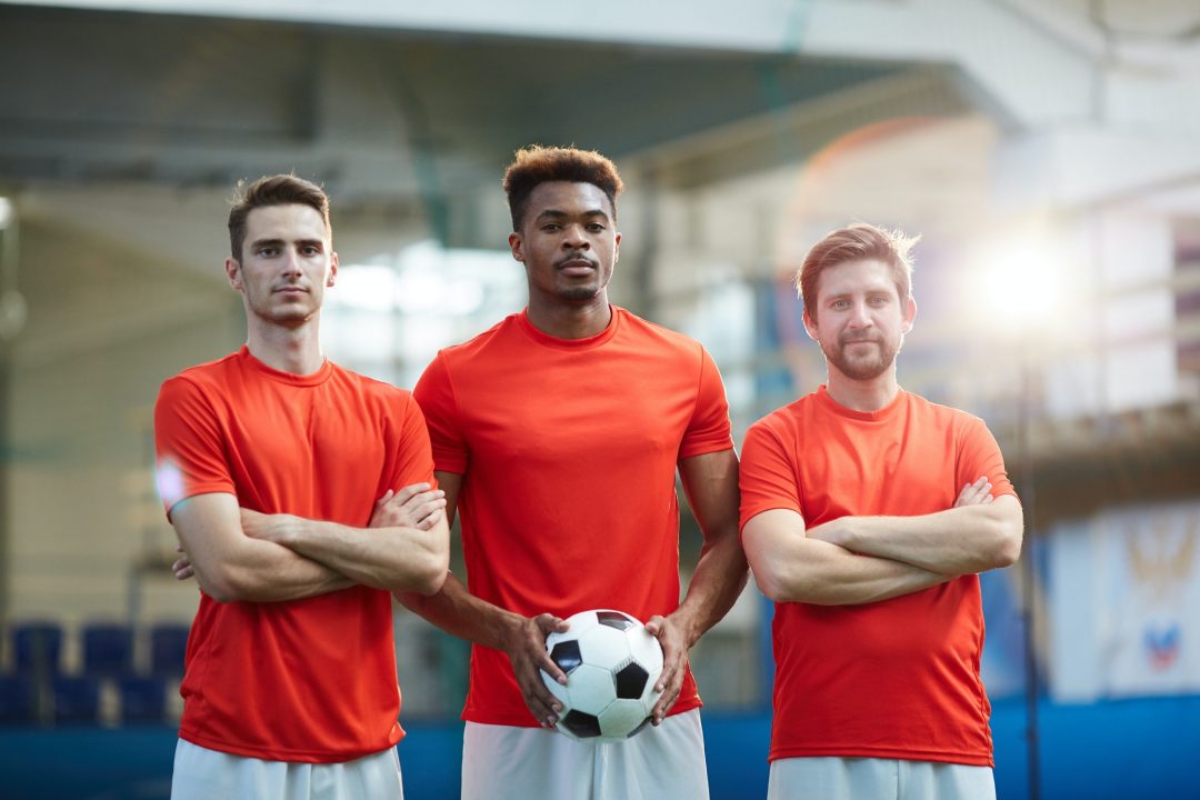Drei Männer in roten Hemden stehen zusammen mit einem Fußball.