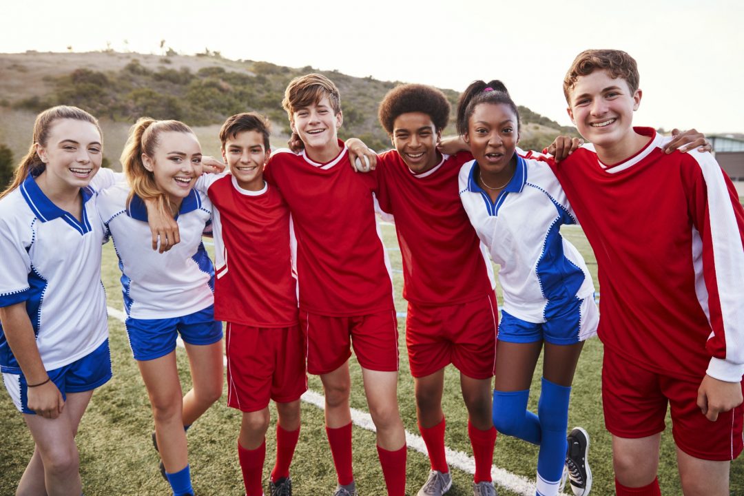 Eine Gruppe junger Menschen in Fußballuniformen steht zusammen und lächelt in die Kamera.