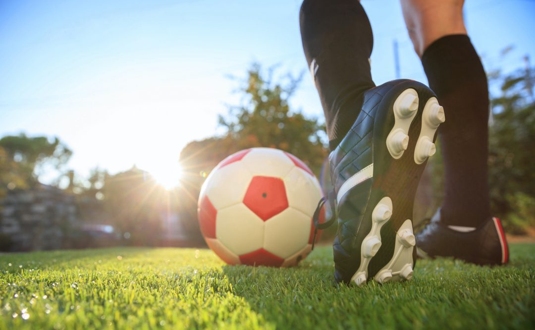 Spieler kickt einen Fußball auf grünem Gras.